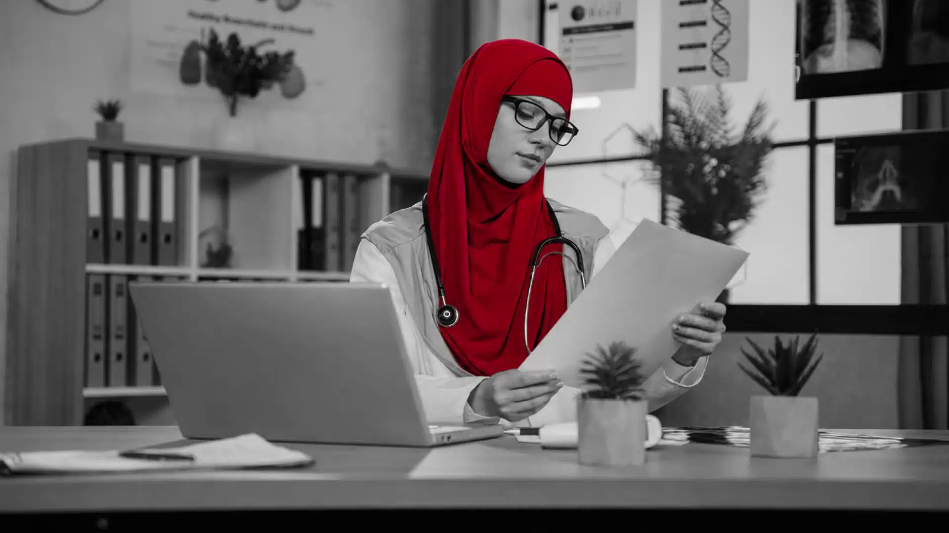 A imagem mostra uma médica, sentada à mesa, em seu consultório, conferindo documentos.